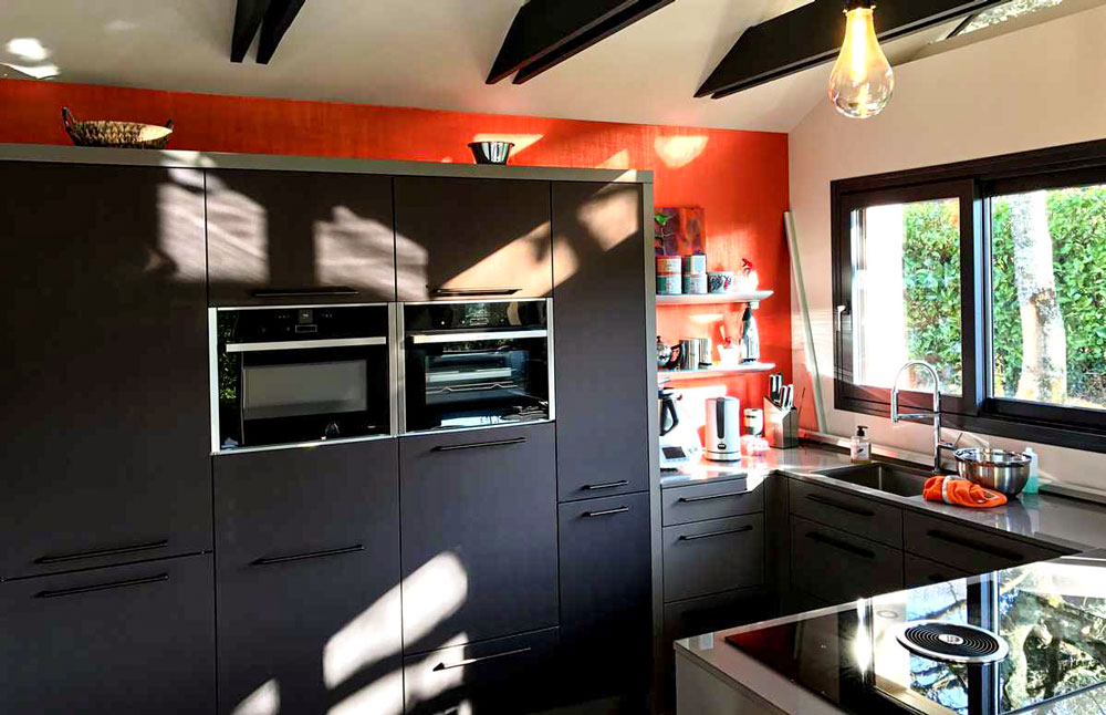 Cette cuisine noire et sobre est égayée par un mur et du mobilier orange
